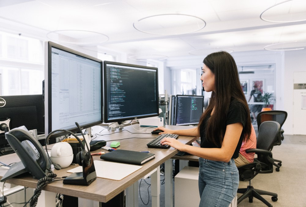 Optiver Graduate- A young female professional working standing infront of her computer.